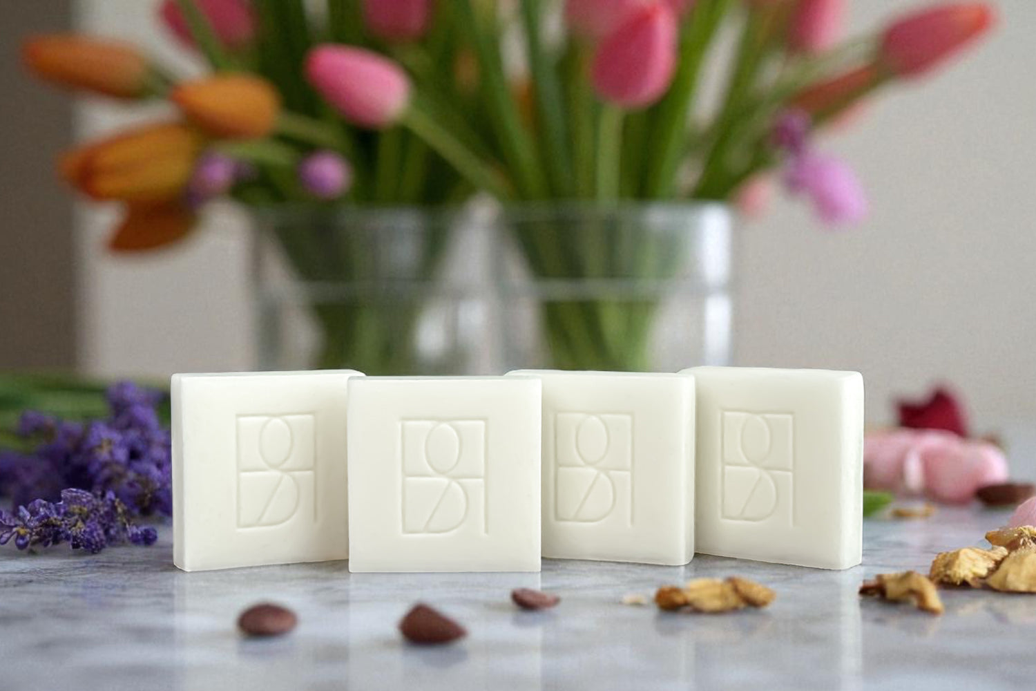 Four wax melts with the Rosie & B monogram on a marble surface, surrounded by flowers and botanicals.