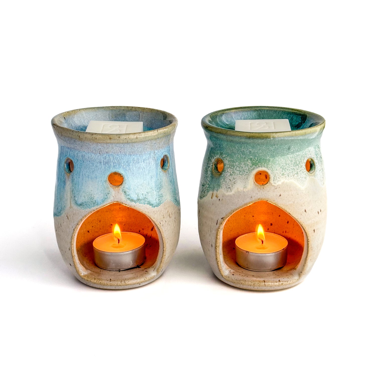 A pair of Leonore ceramic wax melt warmers in Azure Blue & Oatmeal and Hazel Green & Oatmeal, with glowing tealights